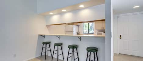 A kitchen with a bar area, three stools, and a white door.