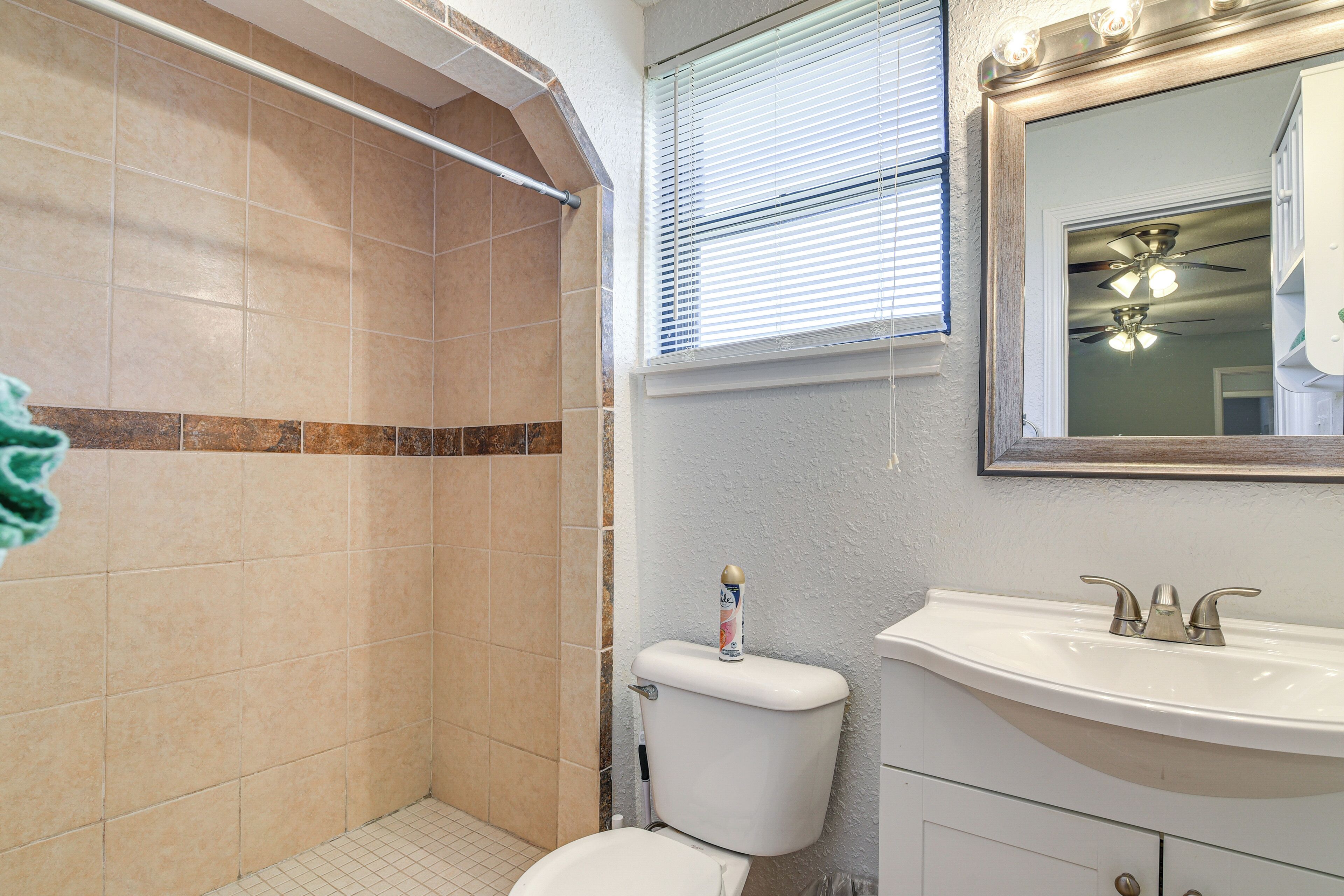 Une salle de bain équipée d’une douche, de toilettes, d’un lavabo et d’un miroir, ainsi que d’un ventilateur de plafond.