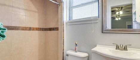 Une salle de bain équipée d’une douche, de toilettes, d’un lavabo et d’un miroir, ainsi que d’un ventilateur de plafond.