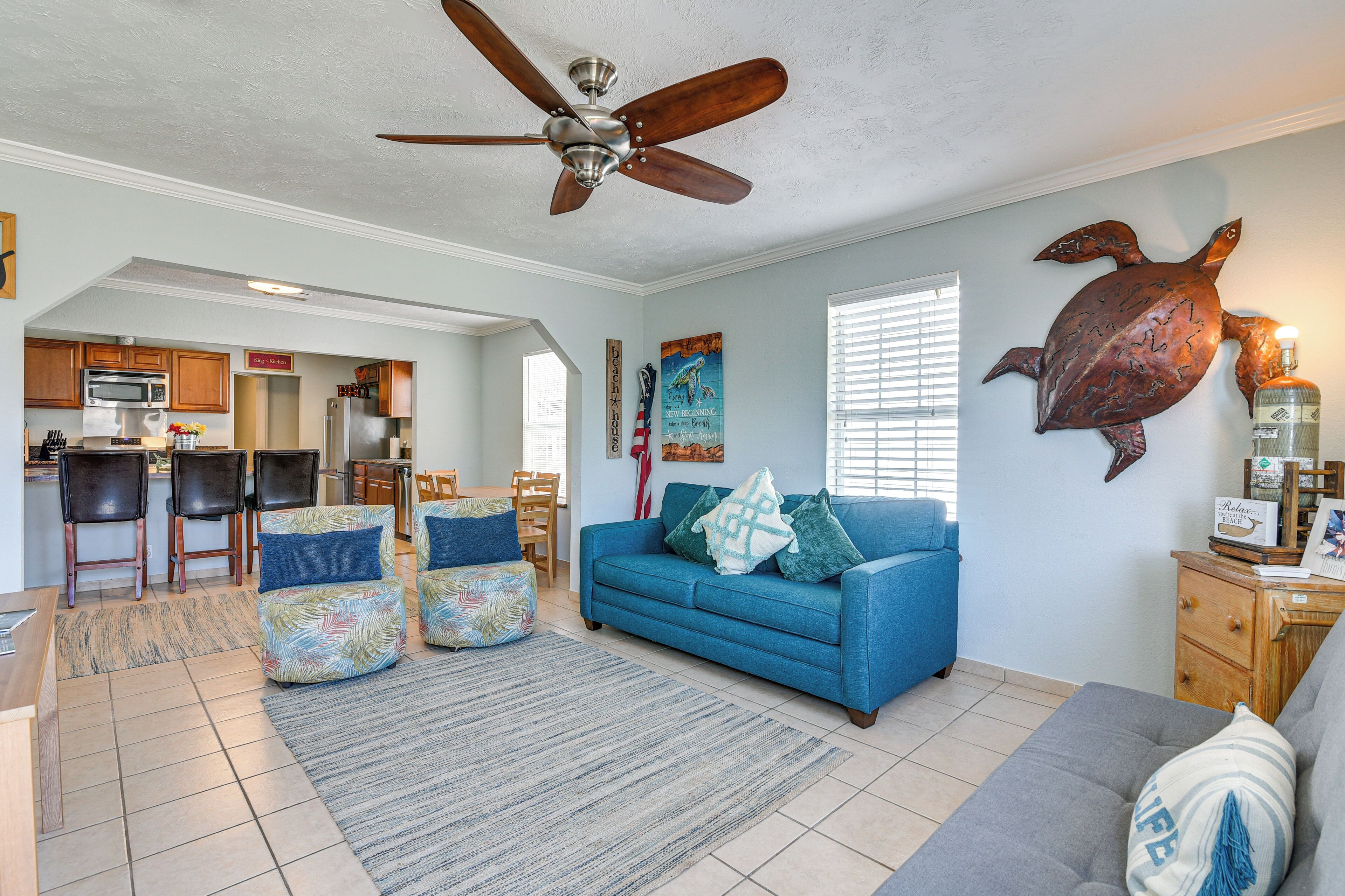 A spacious living room with a blue sofa, a grey couch, and a ceiling fan.