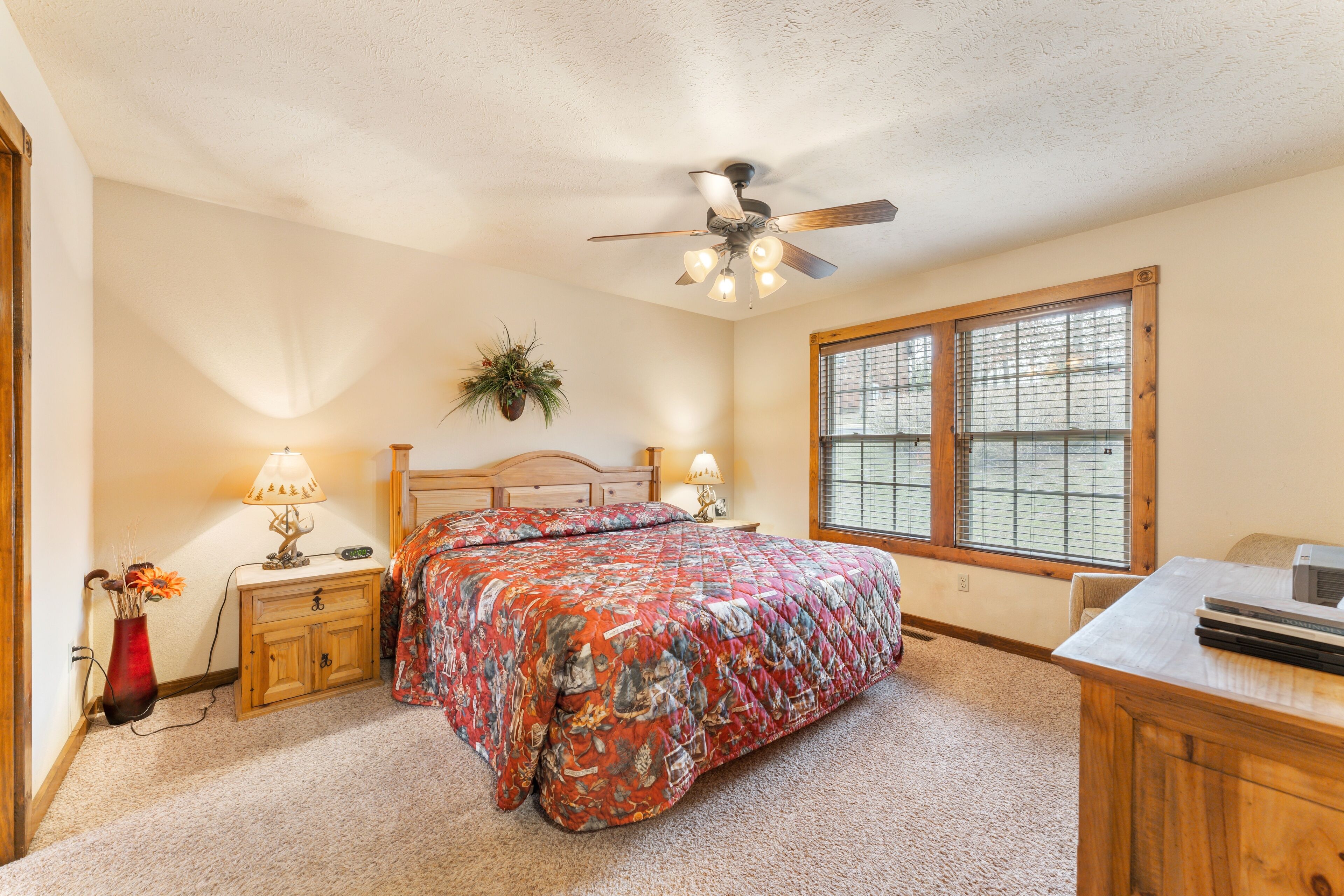 A bedroom with a bed, bedside tables, a desk, a ceiling fan, and a window.
