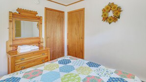A bedroom with a wooden dresser, a mirror, a quilted bedspread, and a wreath on the wall.