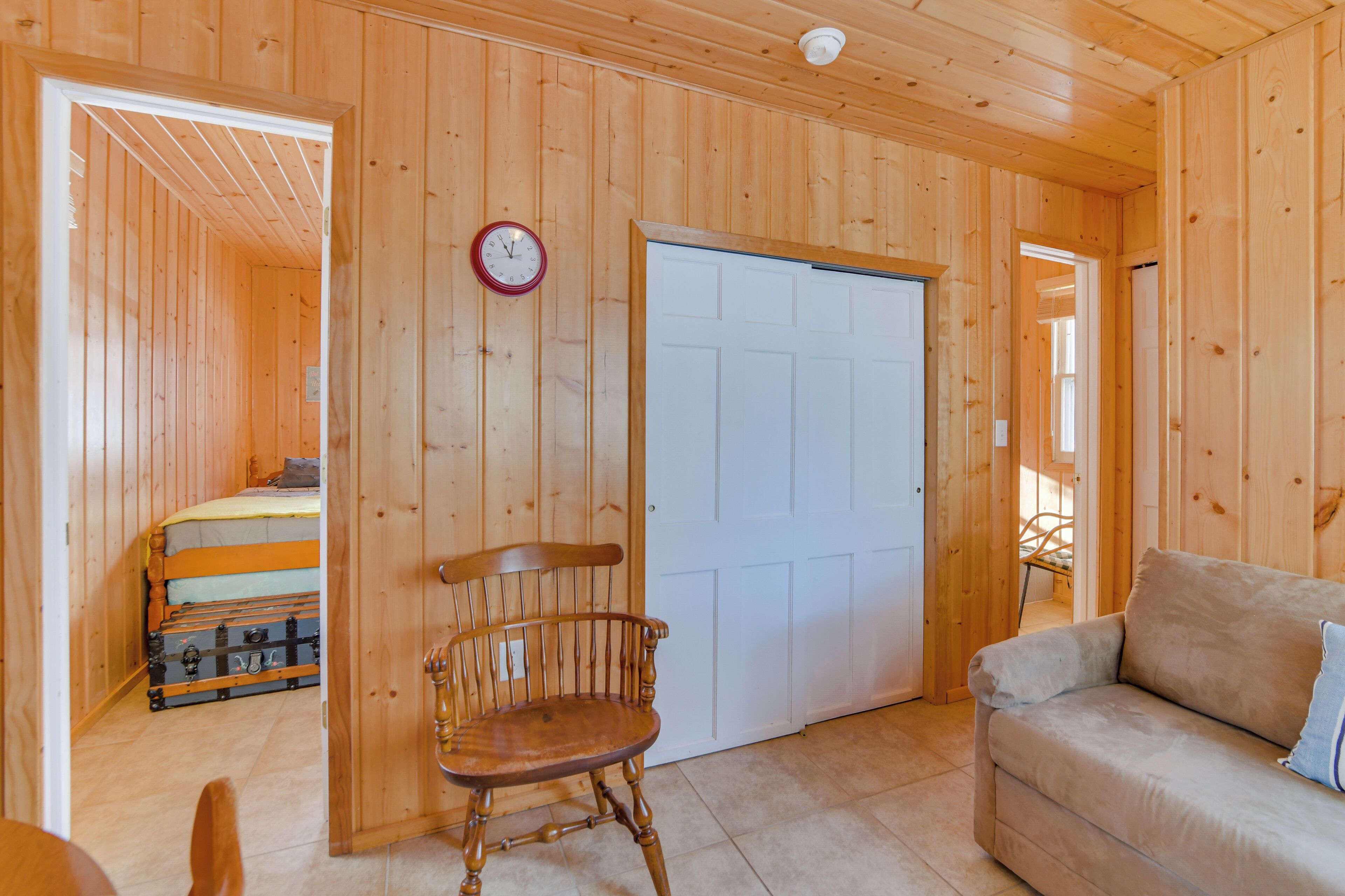 Un interior de madera con una cama, una silla de madera, un sofá y una puerta blanca.
