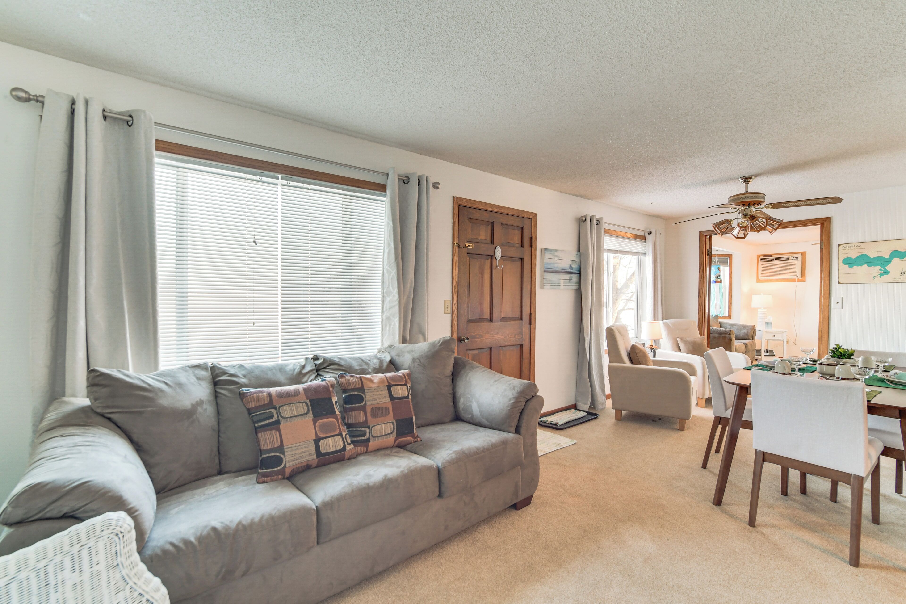 A living room with a grey sofa, a dining table with chairs, and a ceiling fan.