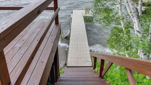 Eine Holztreppe führt zu einem Steg über dem Wasser, umgeben von Bäumen.
