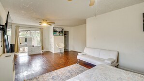 Ein geräumiges Zimmer mit einem großen Bett, einem weißen Sofa, einem Deckenventilator und einem Fenster mit Jalousien.