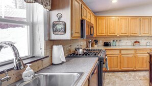 A kitchen with wooden cabinets, a stainless steel sink, a stove, and a window with a view of trees.