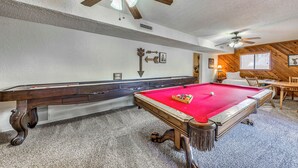 Een biljarttafel in een ruimte met een plafondventilator, houten wanden en een vloerbedekking.