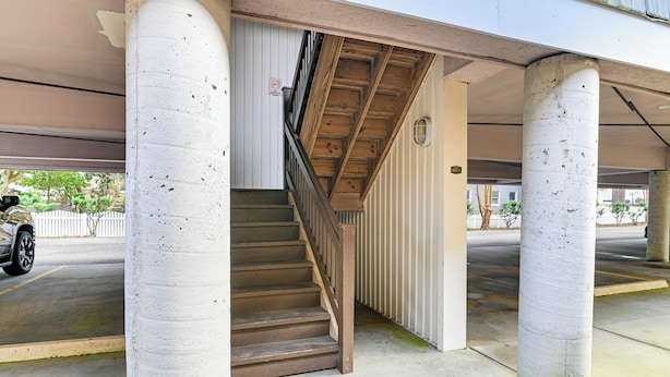 Un parking avec des piliers en béton, un escalier et une voiture garée.