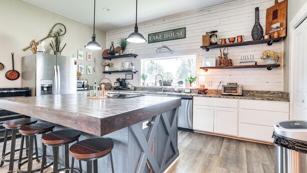 A kitchen with a large island, bar stools, hanging pendant lights, and wooden shelves with various kitchen items. - Pottsboro Home w/ Patio & Grill ~ 1 Mi to Lake! (Pottsboro)