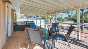 A covered outdoor seating area with wicker furniture and metal chairs, a wooden deck, and a view of a street and trees. - Pottsboro Home w/ Patio & Grill ~ 1 Mi to Lake! (Pottsboro)