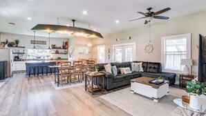 Ein geräumiges Wohnzimmer mit einem dunkelgrauen Sofa, einem Holztisch und einer Essecke mit Holzstühlen und einer Bar.