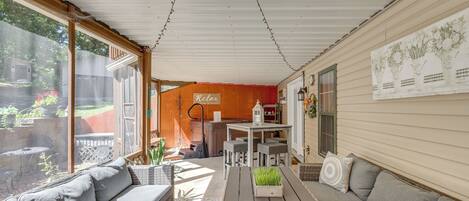 A covered patio with a wooden table, grey sofa, and wicker chairs.