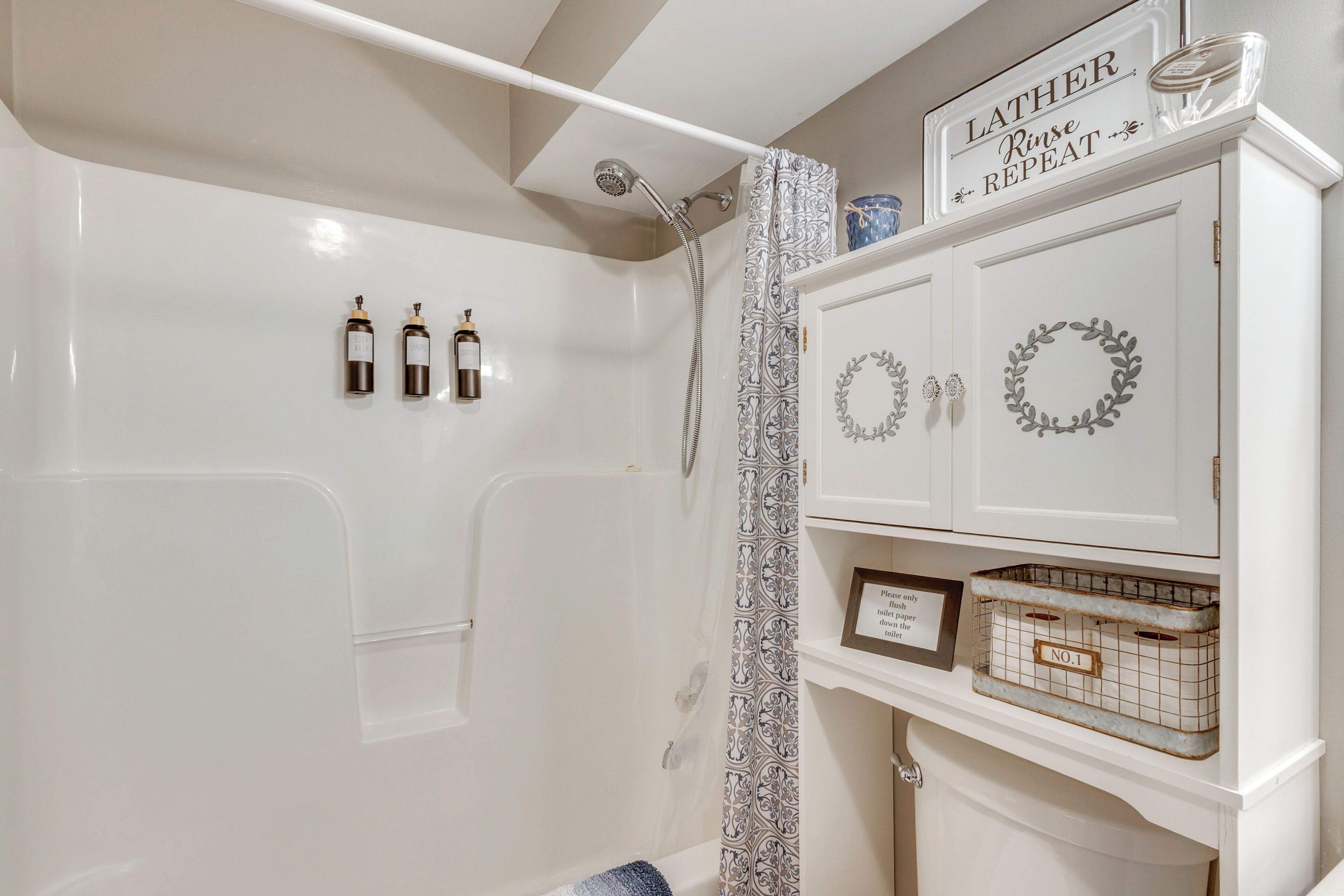 A bathroom with a shower, a vanity with a mirror, and three bottles of shampoo and body wash.