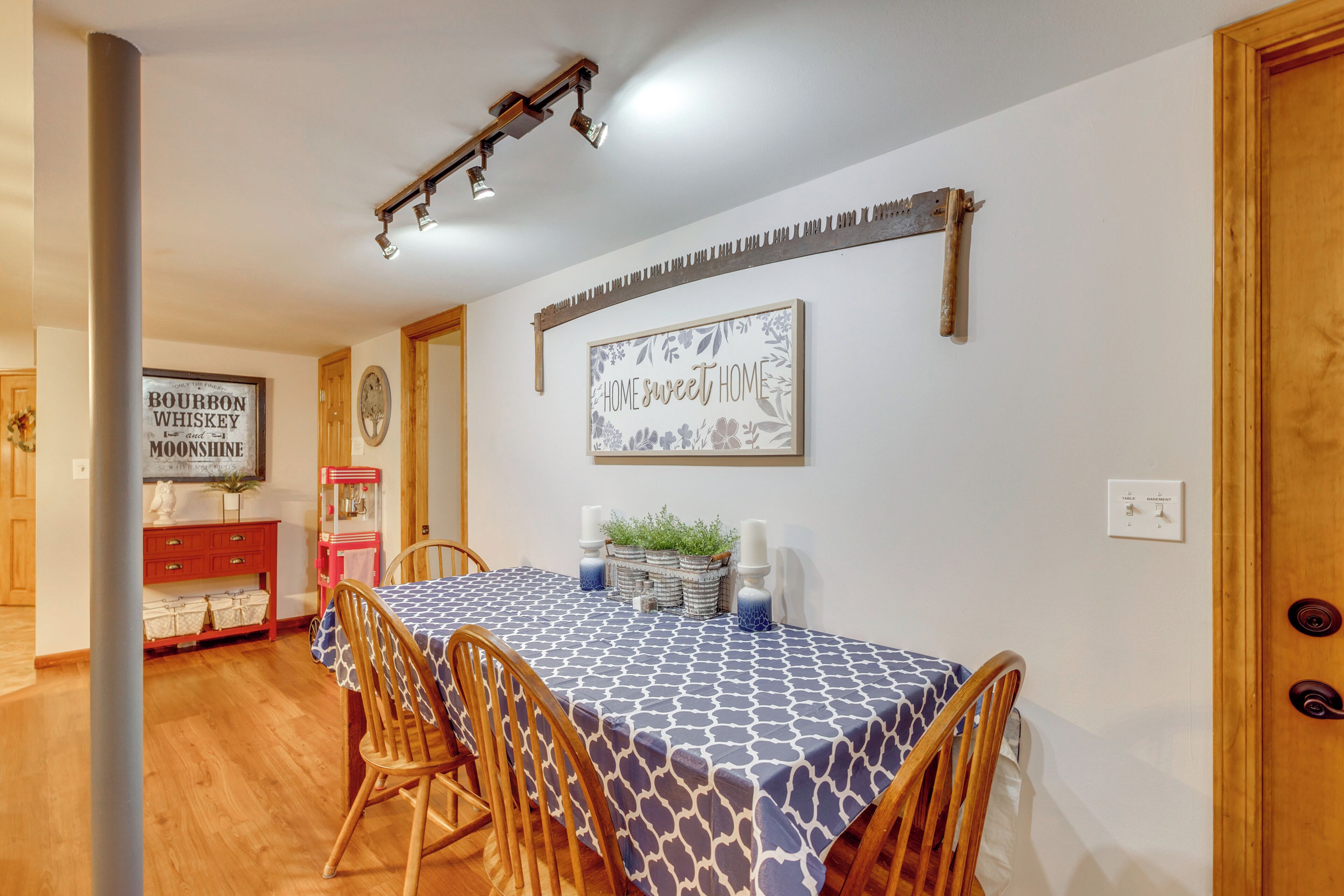 A dining area with a table set for four, wooden chairs, a wall-mounted light fixture, and a sign that reads 'HOME sweet HOME'.