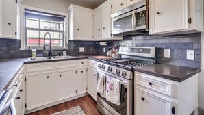 Une cuisine moderne avec des meubles blancs, une cuisinière en acier inoxydable, un four à micro-ondes et une fenêtre équipée de stores.
