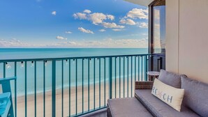Uma varanda com vista para a praia, um sofá com almofada e uma pequena mesa.