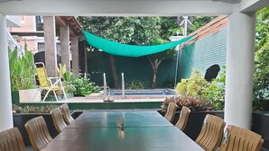 A long wooden table with six chairs, a ceiling fan, and a view of a swimming pool and greenery. - Villa Serenity Le Sejour with Swimming Pool (Puducherry)