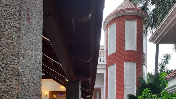 A courtyard with a stone pillar, a red brick building with white windows, and lush green plants. - Villa Serenity Le Sejour with Swimming Pool (Puducherry)