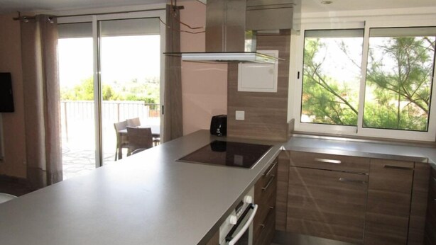 Una cocina moderna con una isla grande, horno empotrado y una puerta corredera de vidrio que da a un espacio exterior.