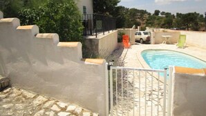 Un área de piscina con un muro de piedra, una reja y un edificio con techo de tejas al fondo.