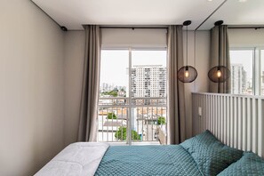 A bedroom with a large window, a bed with teal bedding, and a city view. - Excelente Localização e Conforto Barra Funda - SP - Prox. do Anhembi e Região (Barra Funda São Paulo)