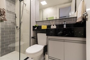 A modern bathroom with a glass shower enclosure, a white toilet, and a black marble countertop with toiletries. - Excelente Localização e Conforto Barra Funda - SP - Prox. do Anhembi e Região (Barra Funda São Paulo)