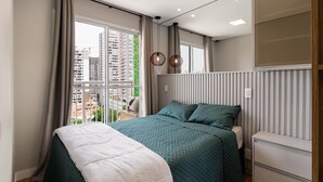 Une chambre moderne avec un grand lit, une table de chevet, un miroir et une fenêtre donnant sur la ville.