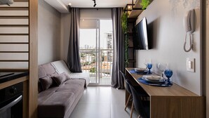 Un appartement moderne doté d’un canapé, d’une table à manger et offrant une vue sur la ville depuis le balcon.