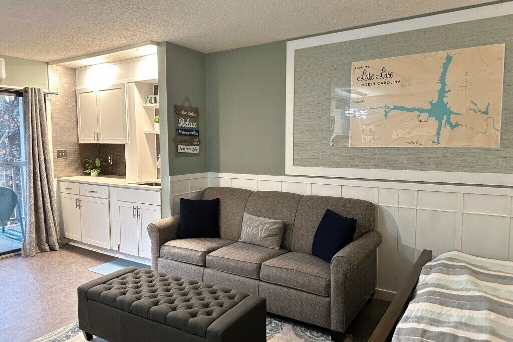Un salon comprenant un canapé, un pouf et une carte du lac Lure, en Caroline du Nord, accrochée au mur.