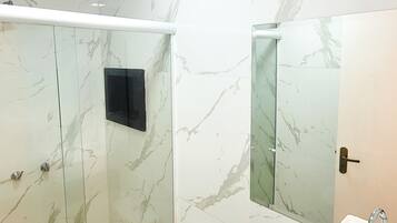 Casa de banho moderna com chuveiro em cabine de vidro, sanita e lavatório com espelho.
