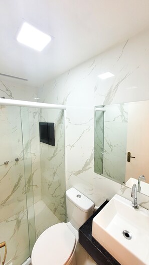 A modern bathroom with a glass-enclosed shower, a toilet, and a sink with a mirror.