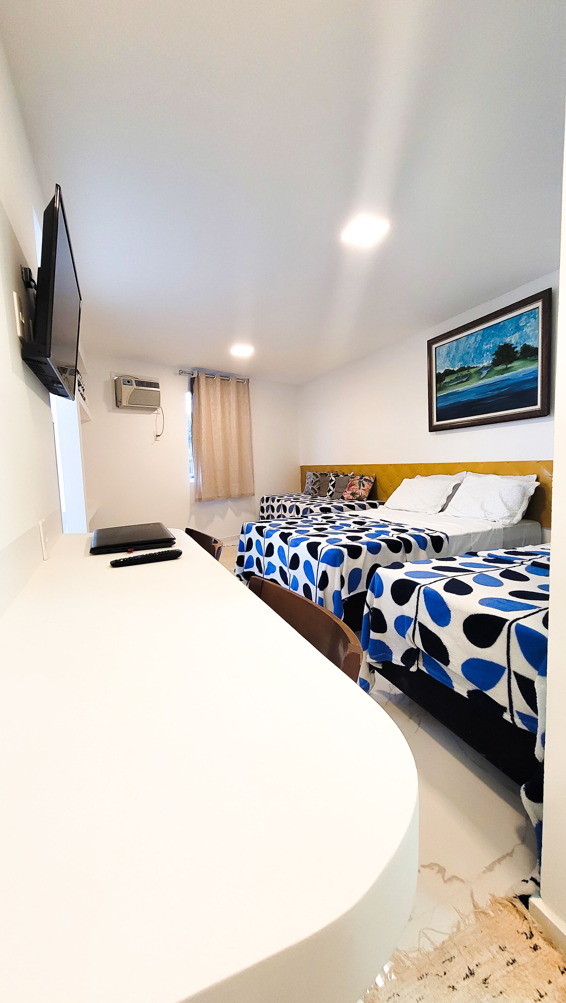 A hotel room with a bed, a desk, a television, and a painting on the wall.