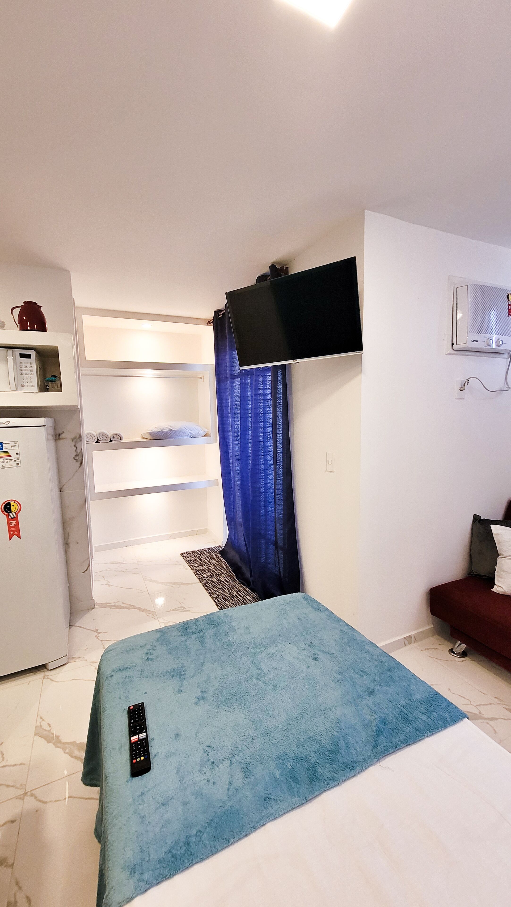 Habitación de hotel compacta con cama, televisor montado en la pared, refrigerador y microondas.