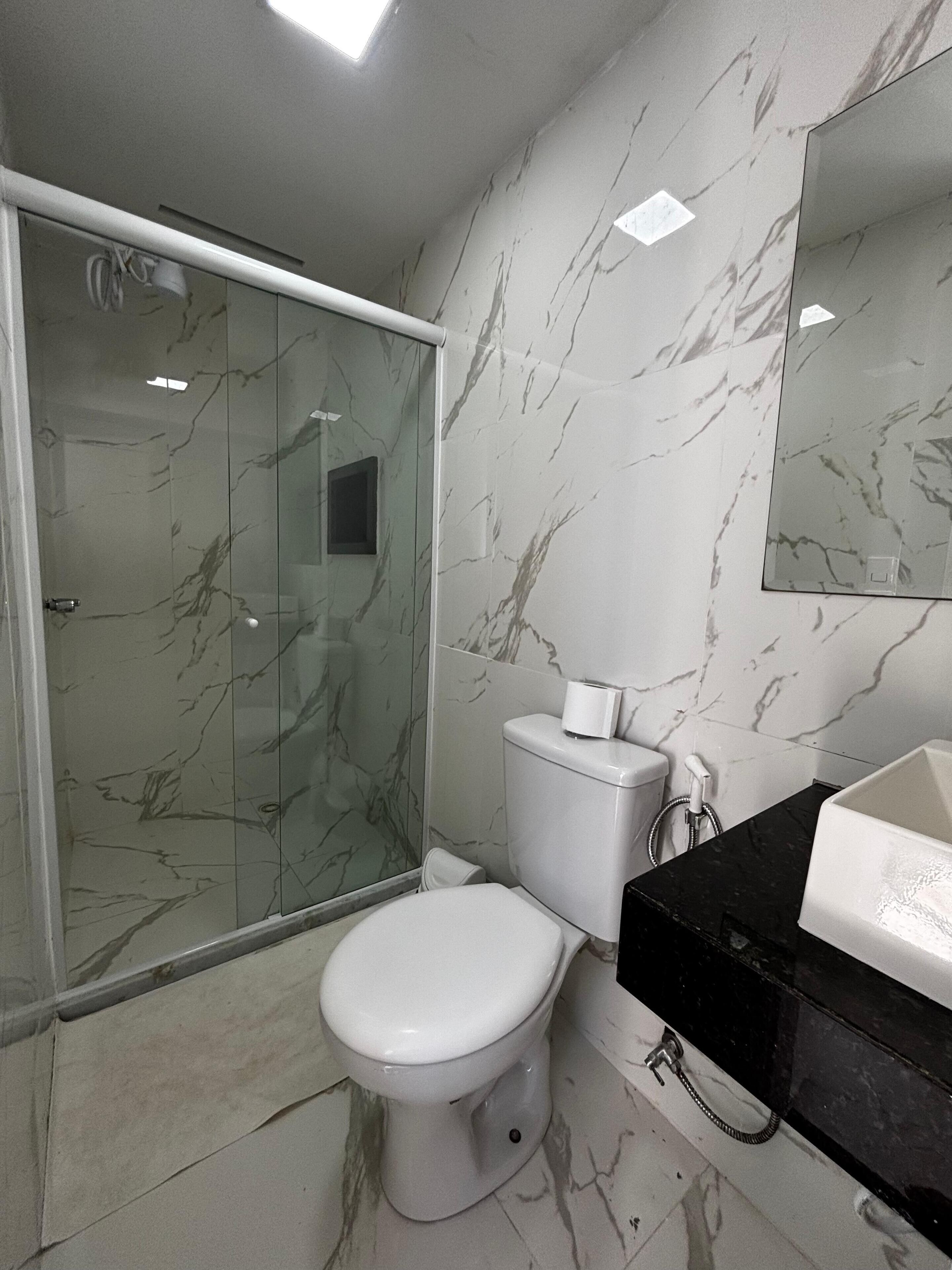 A bathroom with a glass-enclosed shower, a toilet, and a sink with a black countertop.
