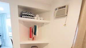 A room with a bed, a suitcase, a shelf with folded clothes, and a radiator. - Flat Jaguanum (Mangaratiba)