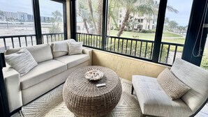 Un balcon avec un canapé, une chaise et un pouf rond en osier.