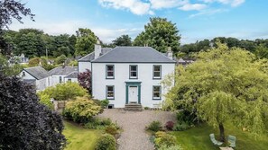 Une maison à deux étages avec un jardin devant, une allée en gravier et un banc.