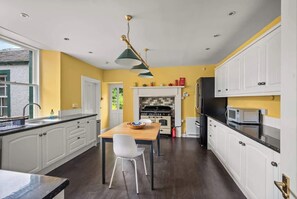 Une cuisine moderne avec des meubles blancs, une table à manger en bois et un poêle noir.