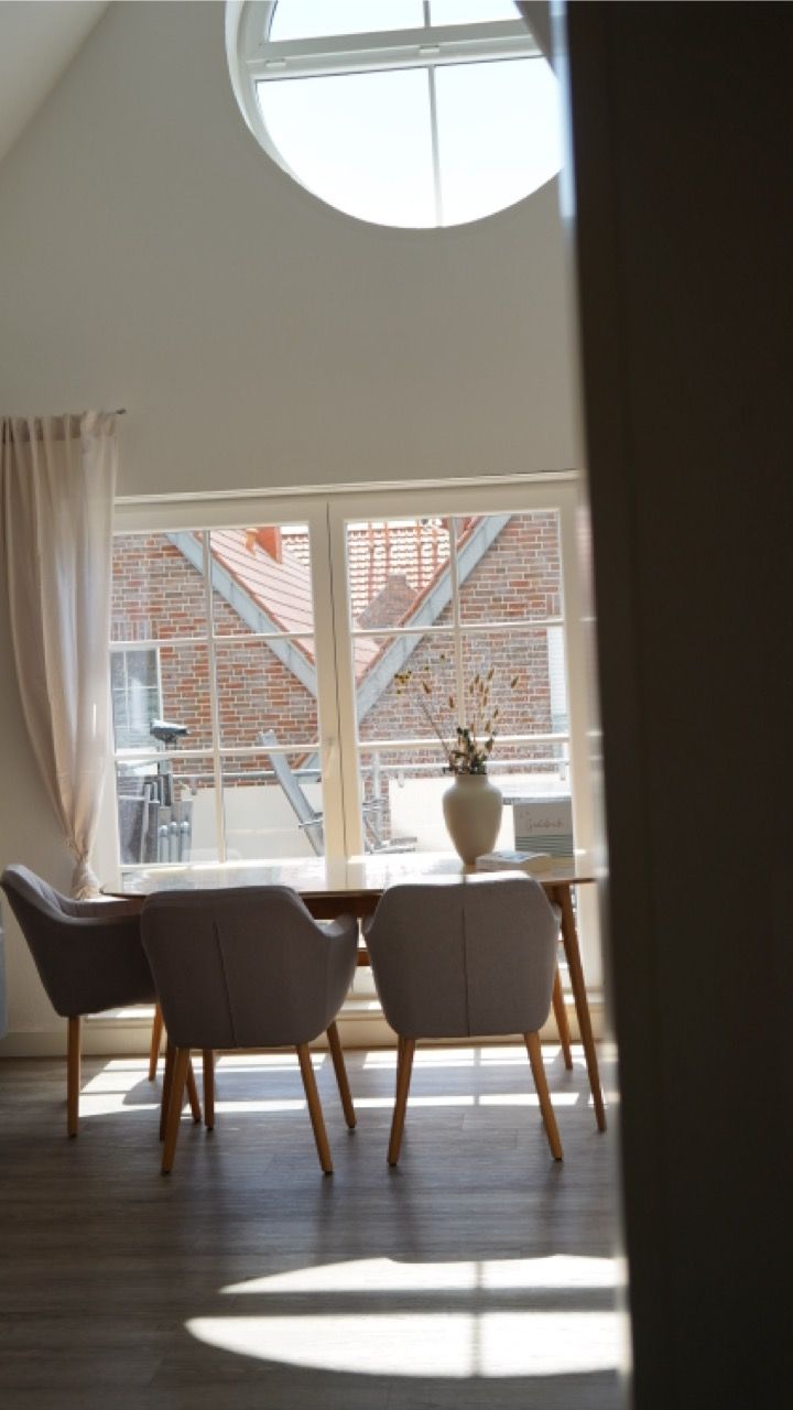 Un coin repas avec une table et des chaises, une fenêtre donnant sur un bâtiment en briques et un vase avec des fleurs sur la table.