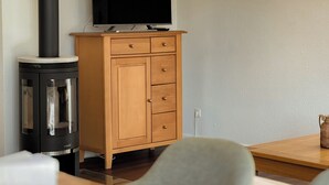 Moderni olohuone, jossa on puinen kaappi, litteänäyttöinen televisio ja musta liesi.