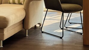 Una sala de estar con un sofá color beige, un sillón verde y una ventana con vista a un edificio de ladrillo.