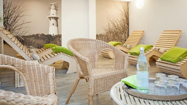 A beachside lounge area with wicker chairs and loungers, a small round table with a bottle and glasses, and a mural of a lighthouse. - Residenz zum Südstrand - Klappke (Borkum)