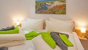 A hotel room with a large bed, two bedside tables, and a painting of a coastal landscape. - Residenz zum Südstrand - Klappke (Borkum)
