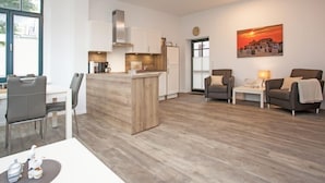A modern living room with a wooden coffee table, two armchairs, a sofa, and a dining area with a white table and chairs. - Residenz zum Südstrand - Klappke (Borkum)