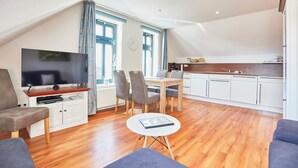 A modern living room with a flat-screen TV, a dining table with chairs, a small coffee table, and a kitchen area with white cabinets and a wooden countertop. - Villa Wilhelmine - Klein-wiebke (Borkum)