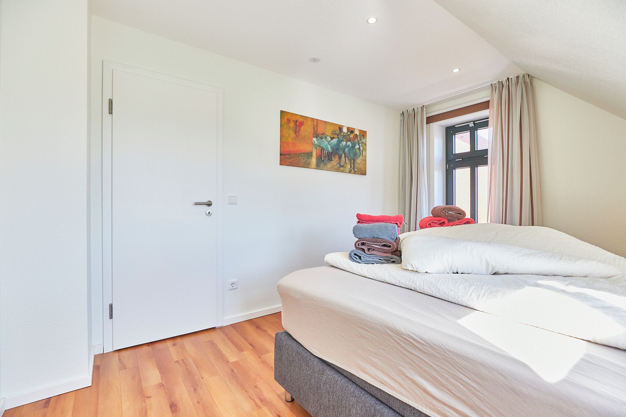Une chambre à coucher avec un lit, une porte, un tableau et une fenêtre avec des rideaux.