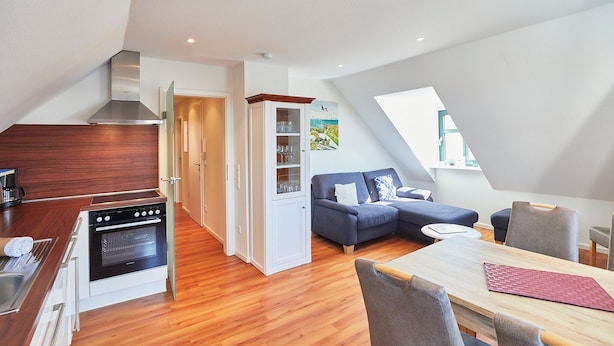 A modern kitchen with built-in appliances, a dining area with a wooden table and chairs, a blue sofa, and a view of the outdoors through a skylight. - Villa Wilhelmine - Klein-wiebke (Borkum)