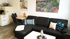 Ein modernes Wohnzimmer mit einem schwarzen Ecksofa, einem weißen Couchtisch und einem Essbereich mit Holztisch und Stühlen.