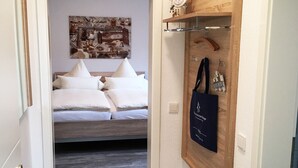 Ein Schlafzimmer mit einem Bett, einem Wandbild und einem Holzregal mit einer Uhr und einer Tasche.